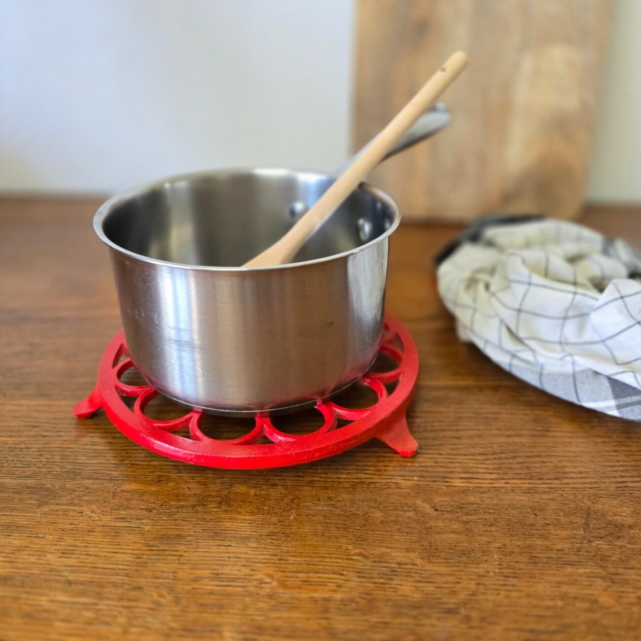 Dessous de plat ajouré en fonte rouge avec casserole et cuillère en bois – mise en scène cuisine rétro authentique
