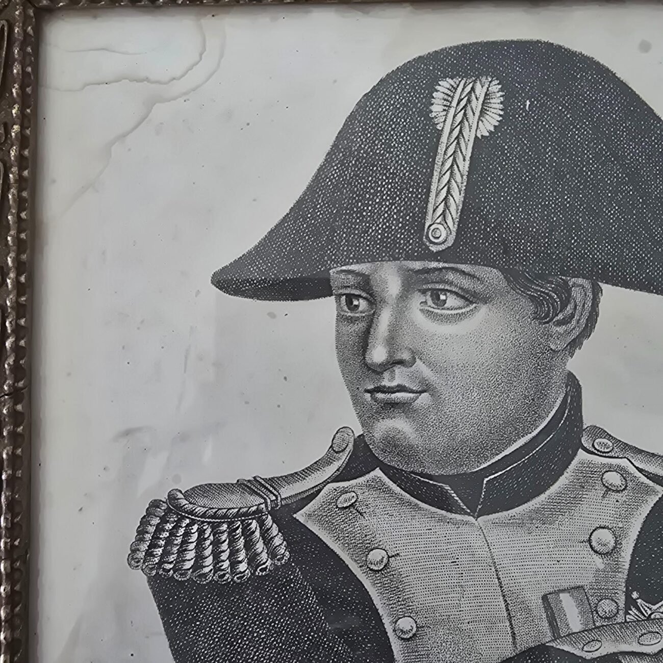 Zoom sur le haut gauche du visage de Napoléon avec son bicorne et les détails du cadre ancien.