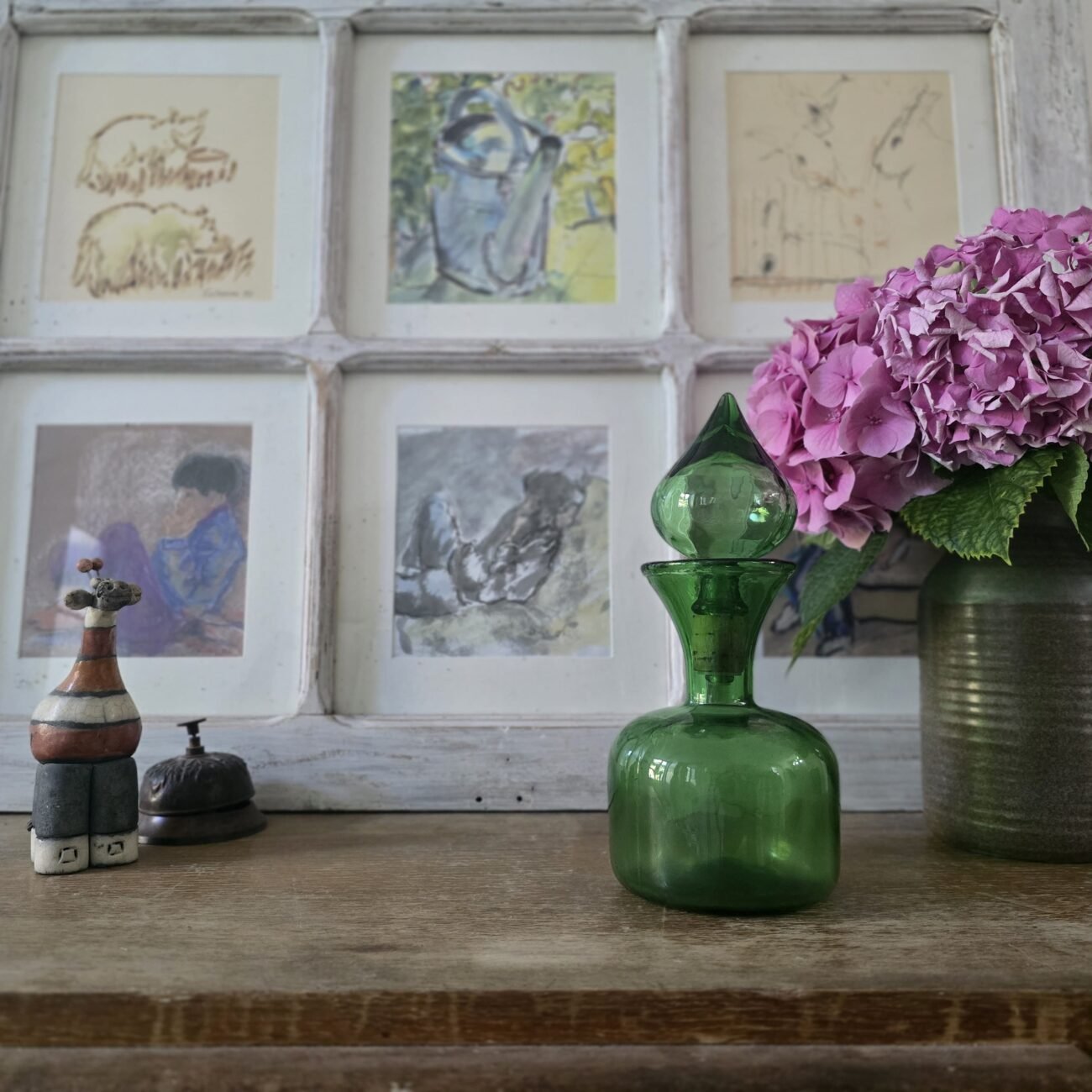 Scène décorative avec la carafe verte et objets d’art autour.