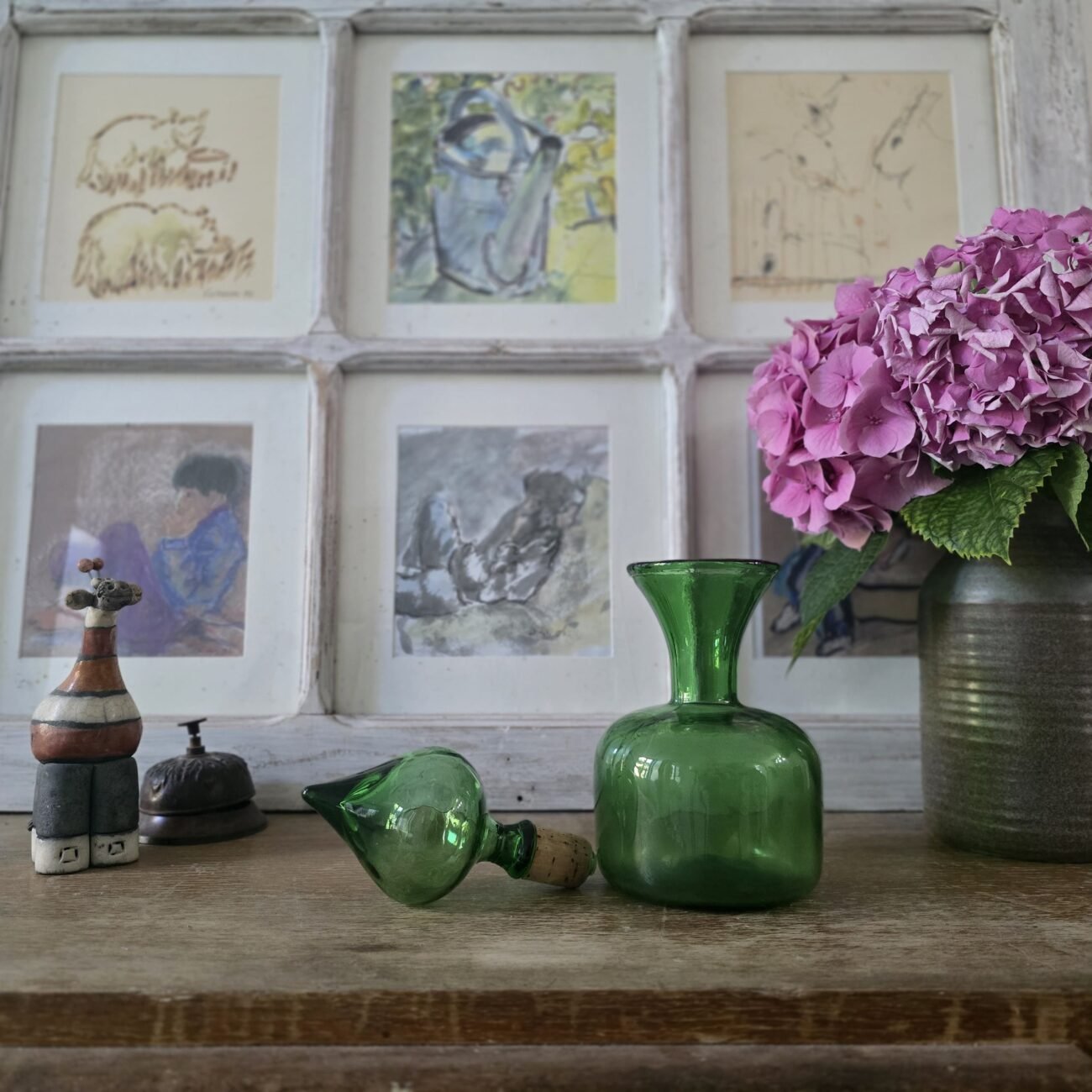 Carafe en verre vert bouchon à côté, cadrée sur une composition florale.