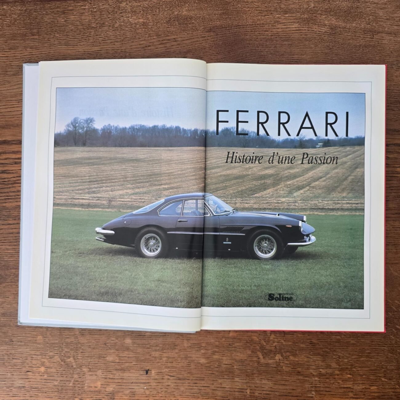 Double page intérieure présentant une Ferrari ancienne noire en pleine campagne
